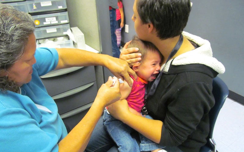 A photo of a woman holding her daughter as she receives seven vaccine shots.