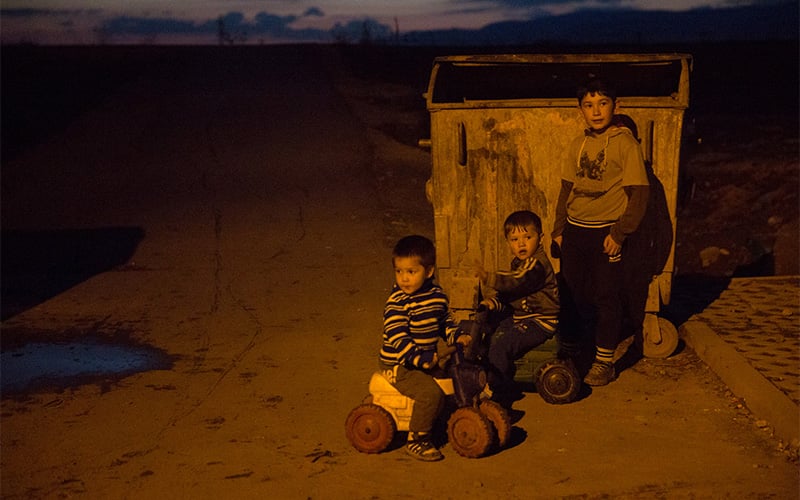Three boys play near a dumpster as night falls in the Slovakian Gypsy ghetto.