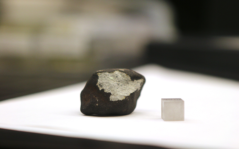 The largest of the fifteen meteorites next to a one-centimeter cube for scale. The black outer later is called a “fusion crust” and forms when the outside melts as the objects falls hurtles through the atmosphere at high velocity. (Photo by Anna Copper/Cronkite News)