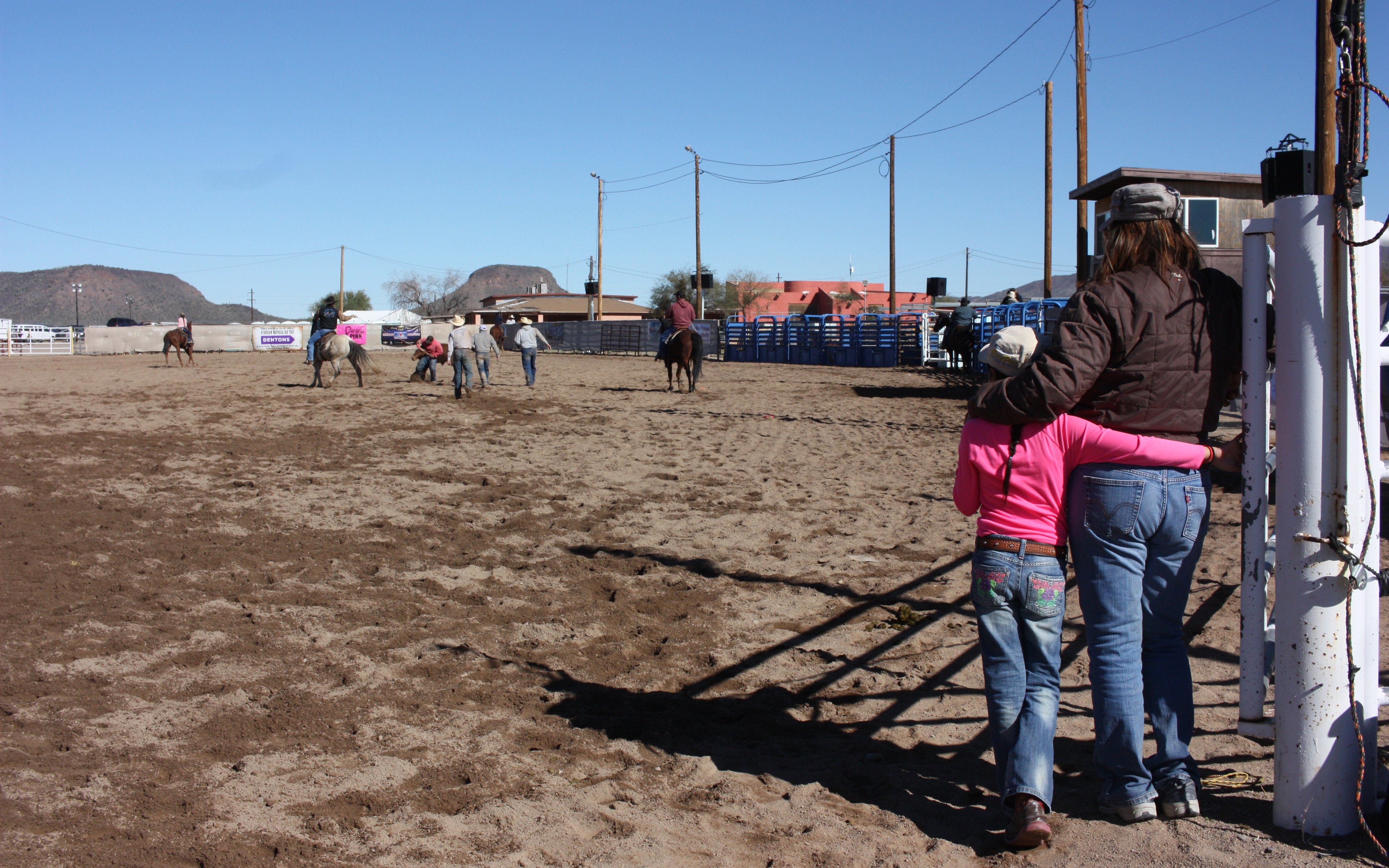 Constance Benally and her daughter Angelina Begay, 8, watch participants practice before the All Indian Rodeo Open Show  Saturday. Three of her daughters were in the Junior Rodeo. (Photo by Sarah Jarvis/Cronkite News) 