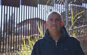 Carlos Santa Cruz, a landscaper who lives near the wall in Nogales, AZ, stands in front of the border wall in Nogales on January 25, 2016. (Photo by Josh Orcutt/Cronkite News)