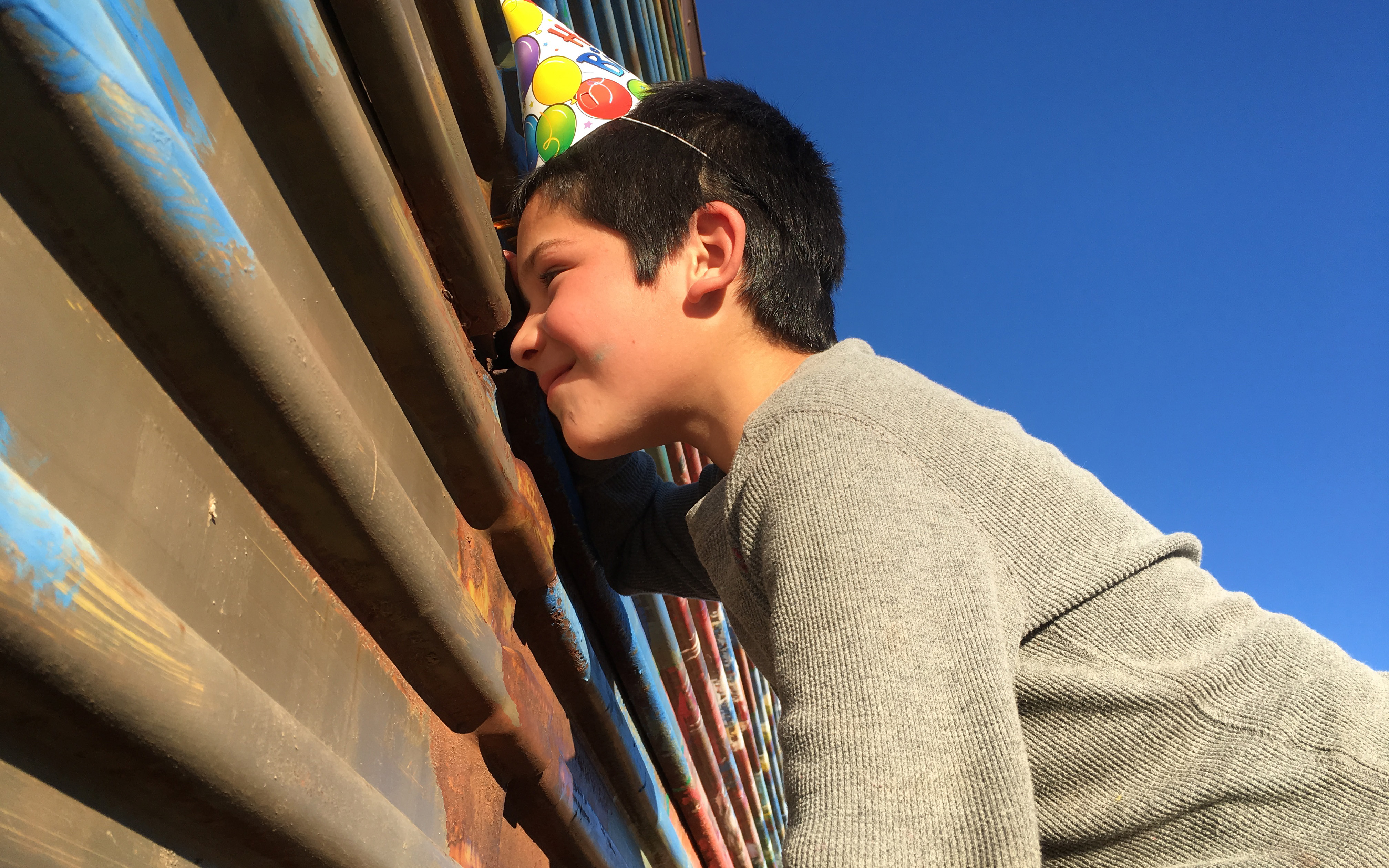 Martin Romero Rodriguez, a young artist with Border Bedazzlers, peeks through a hole in the border fence. He and other kids in Naco, Sonora gathered recently for a party to bid farewell to the mural they painted on the barrier. (Photo by Charlene Santiago/Cronkite News)