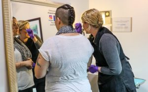 Salong owner Adele LaVoie, wearing purple gloves, demonstrates how to care for your eyebrows after microblading. (Photo by Saeed Alshamisi/Cronkite News)