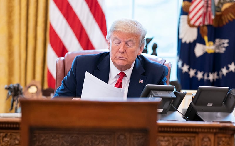 President Trump sits in Oval Office, reading a printed memo.