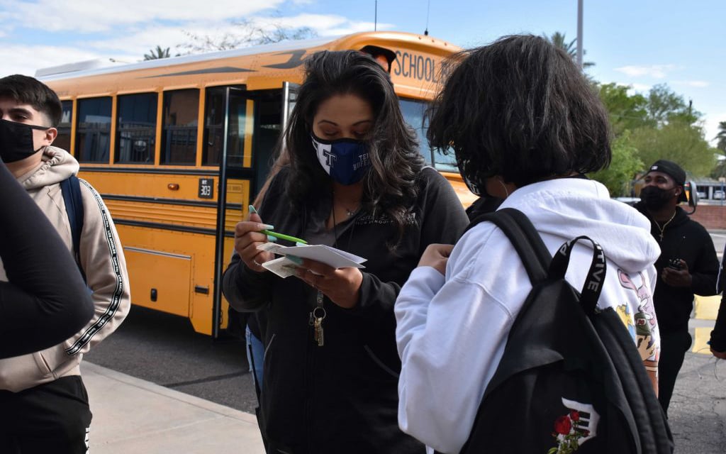 A masked school official talks with a student