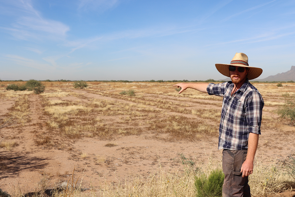 Grant Tims points out an area heavily affected by desertification. The sparse areas of tall grass are caused by rapid evaporation of rainwater after it rolls off unhealthy soil. (Photo by Brock Blasdell/Cronkite News)
