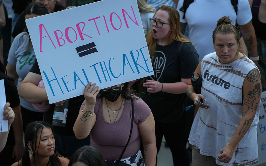 woman holding "abortion equals healthcare" protest sign in crowd