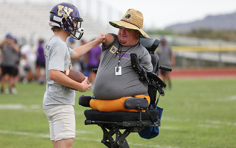 Wickenburg assistant coach Carter Crosland, who was diagnosed with Tetra-Amelia syndrome at birth, takes a 40-minute ride on his motorized wheelchair to football practice. (Photo by Grace Edwards/Cronkite News)