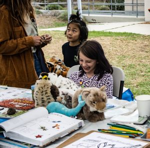 Kids smile at P-22 festival. Table with stuffed animals, arts and crafts activity. Photo taken on Oct. 22, 2022. (Photo by Emeril Gordon/Cronkite News)