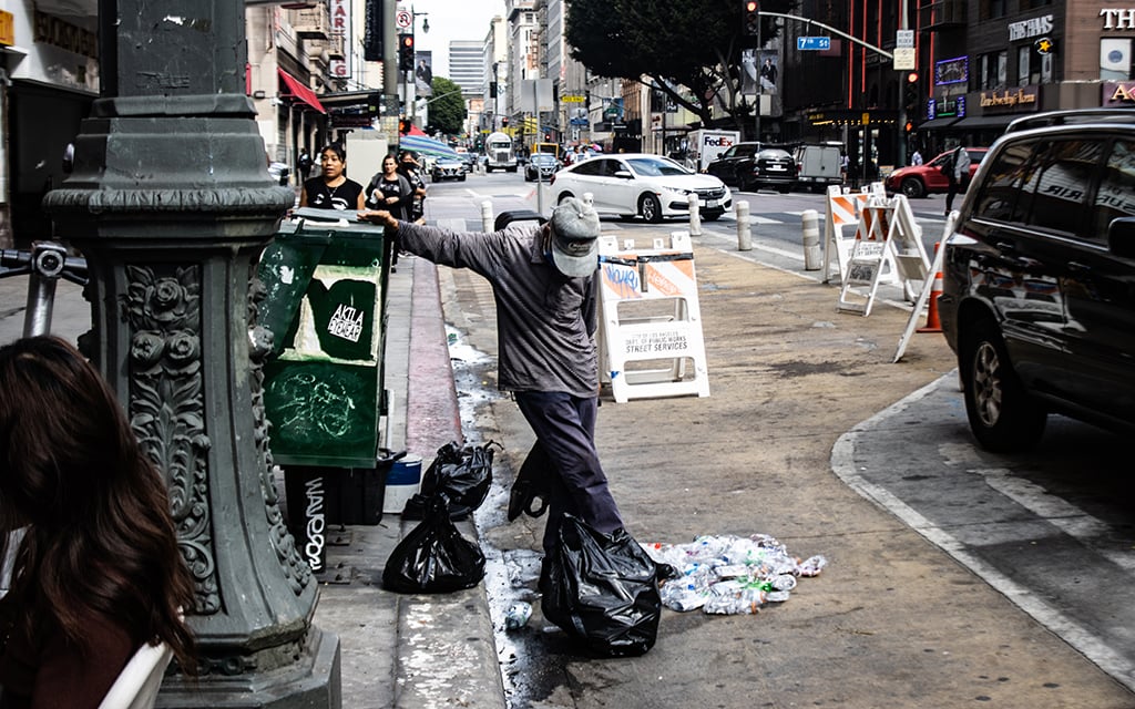 A man crushes cans and containers that can be cashed in at recycling centers. Scavengers go through some of the garbage left curbside Los Angeles. The city faces big problems of trash left on streets. (Photo by Emeril Gordon/Cronkite News)