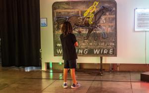 A patron examines a restored racetrack sign at the Museum of Neon Art in Glendale, California, on Sept. 16. (Photo by Emeril Gordon/Cronkite News)