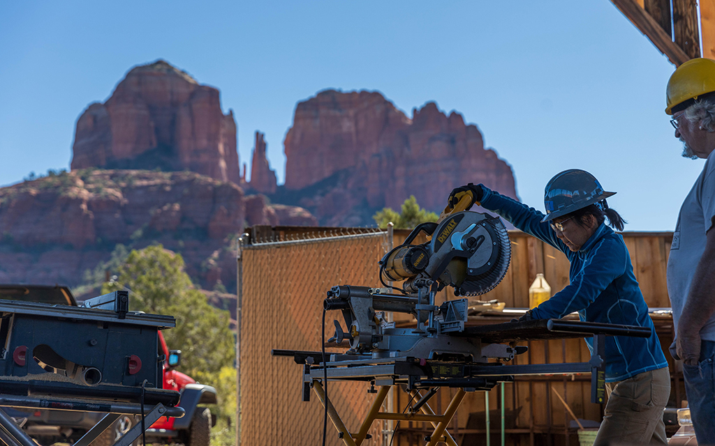 HistoriCorps volunteer Yumi Shimizu, left, learns how to use a circular saw from project supervisor Pete Specht on Oct. 24, 2022, with Sedona’s Cathedral Rock as a picturesque backdrop. (Photo by Drake Presto/Cronkite News)