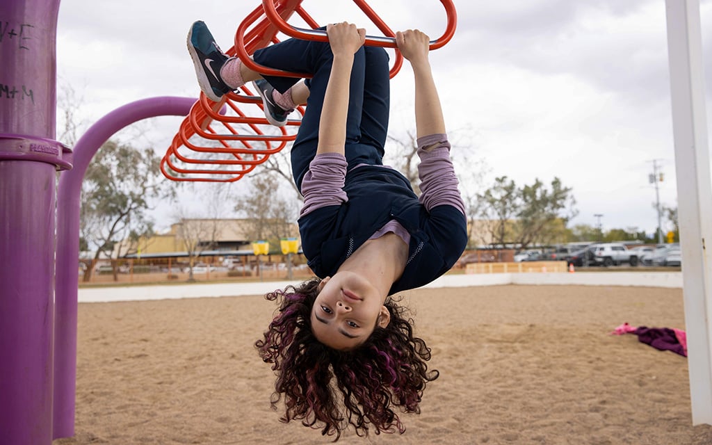 Rebekah Gonzales, 11, plays on the monkey bars at Loma Linda Elementary School in Phoenix while she waits for the new playground unveiling. Her biggest wish for the new playground was for it to have a zip line, which it does. Photo taken on Feb. 23, 2023. (Photo by Evelyn Nielsen/Cronkite News)