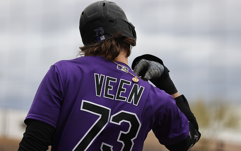 Zac Veen's name and number are visible on the back of his baseball jersey, and a gold chain with a smiley face pendant hangs over his shoulder.
