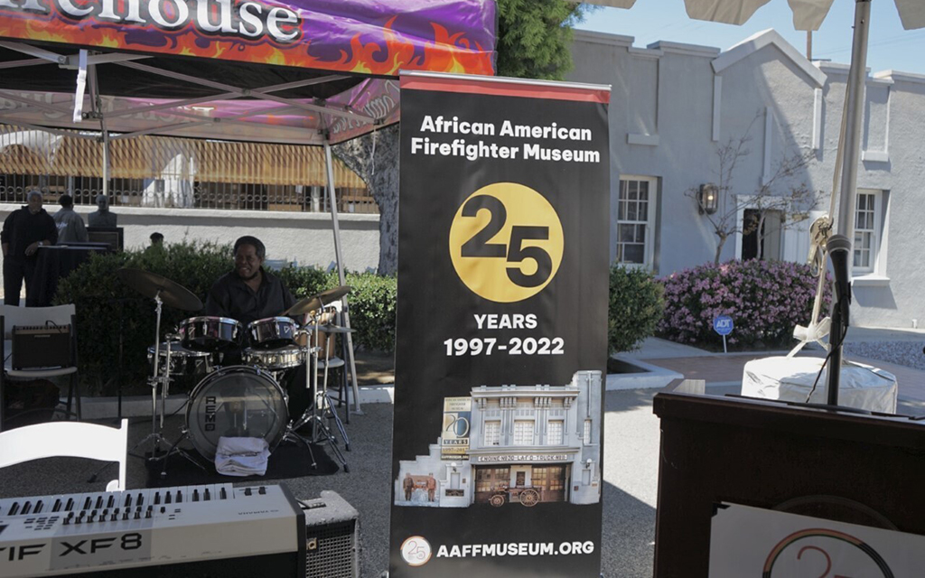 A band plays outside in front of a banner for the African American Firefighter Museum's 25th anniversary.