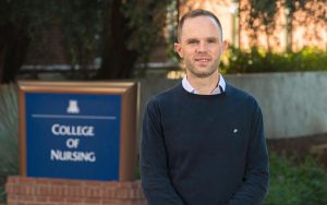 Thaddeus Pace poses for a photo in front of a sign for the UArizona College of Nursing.