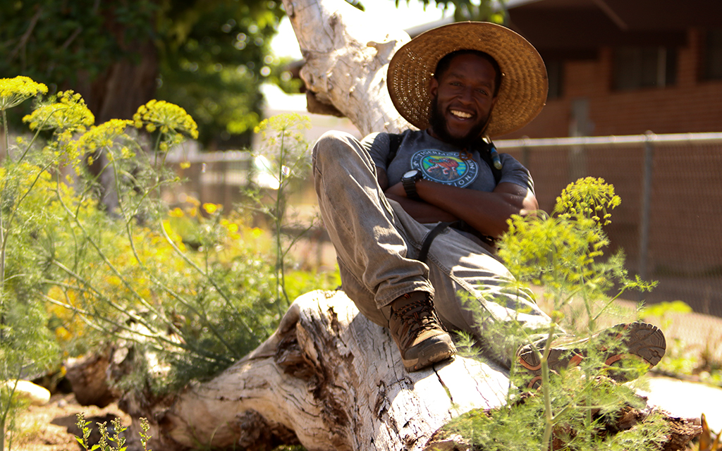TigerMountain Foundation garden manager Rodney Smith poses on a tree surrounded by parsley at the foundation's community gardens on April 25, 2023. (Photo by Logan Camden/Cronkite News)
