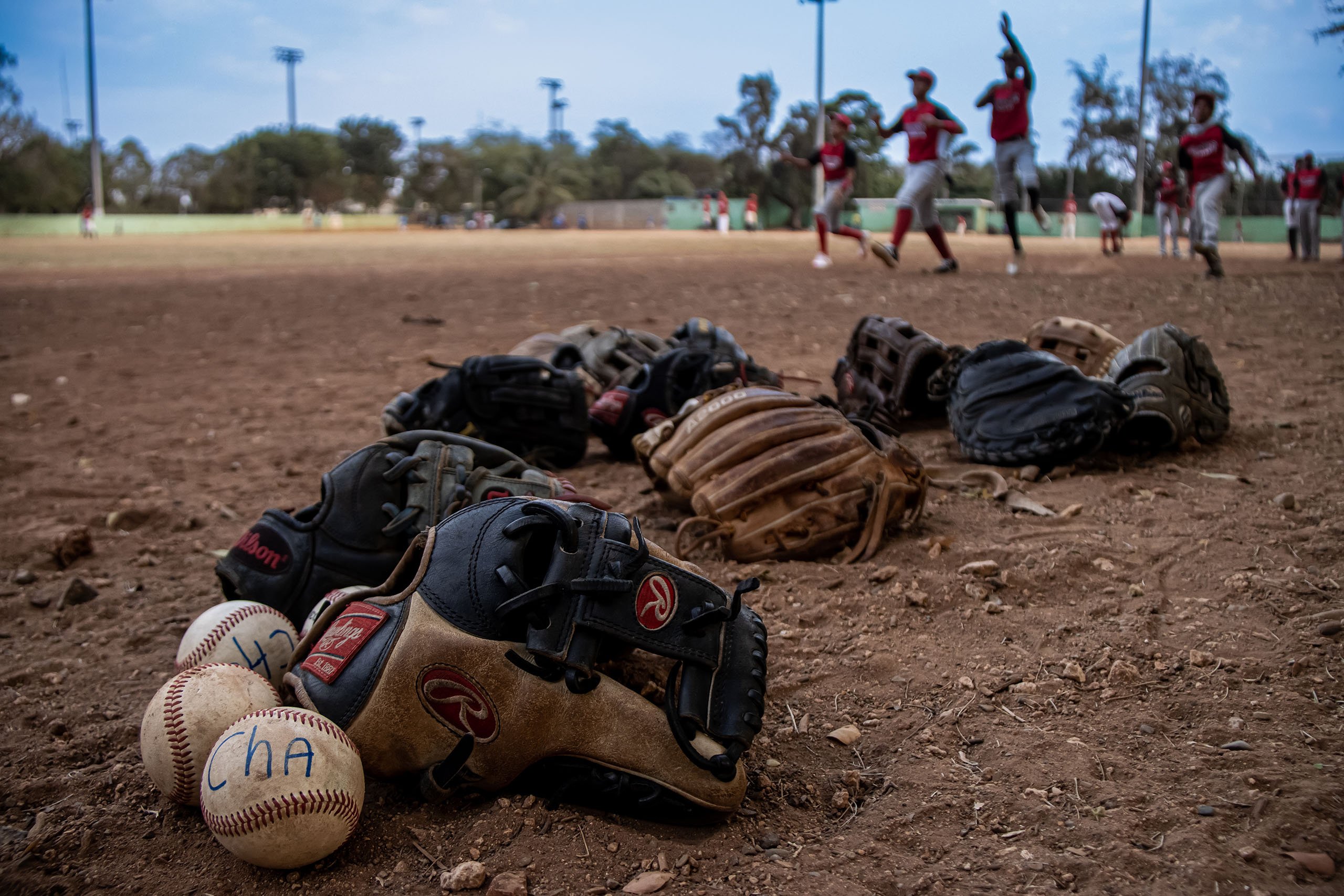 Leones D’Chaca League players leave their equipment on the ground while they warm up before starting play at the Félix Sánchez Olympic Stadium in Santo Domingo, Dominican Republic, on March 8, 2023. (Photo by Trilce Estrada Olvera/Cronkite Borderlands Project)
