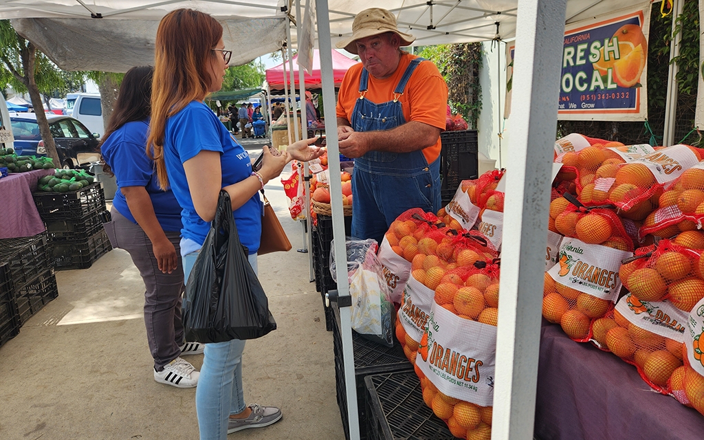 Brian Griffith, right, sells oranges to patrons at the farmers market at Central Avenue and 43rd Street in Los Angeles. Griffith accepts Market Match funds, which help SNAP recipients extend their food budget. (Photo by Taylor Ens/Cronkite News)