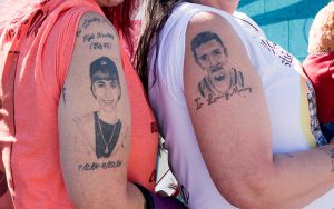 New Mexico Crusaders for Justice co-founders Sally Sanchez and Josette Otero show tattoos of their sons, who both died as a result of gun violence. They attended the unveiling of a mural from New Mexicans to Prevent Gun Violence outside San Pedro Library in Albuquerque on Nov. 4, 2023. (Photo by John Leos/Cronkite News)