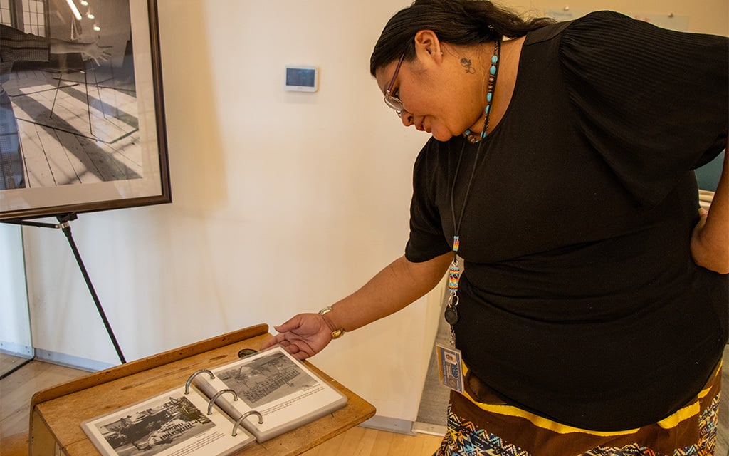 Elena Selestewa, a visitors center specialist at Native American Connections and Phoenix Indian School, reads through a photo book of historical records and experiences from Phoenix Indian School. (Photo by Ellie Willard/Cronkite News)
