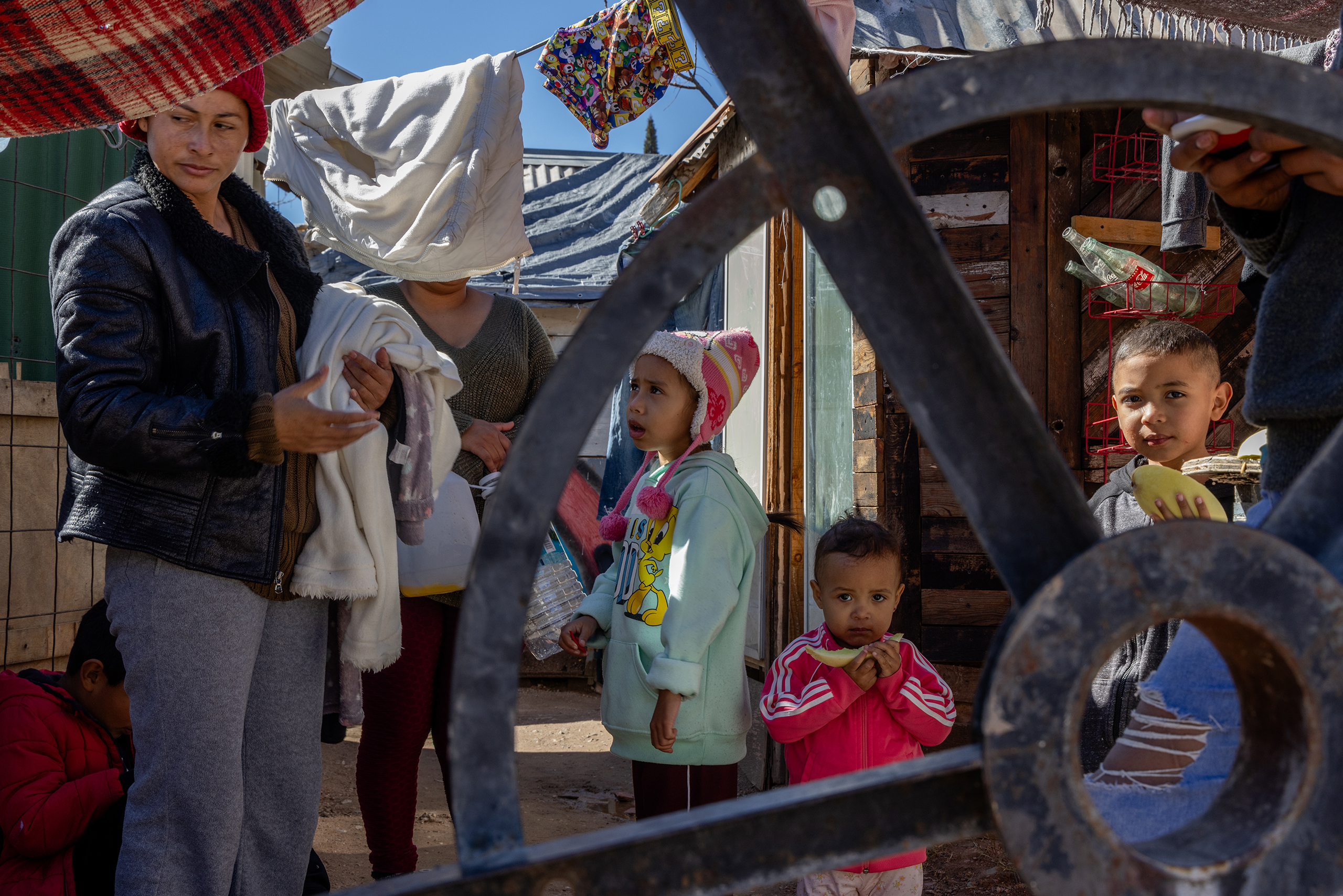 A family of migrants, including, from left, Ruth Barrera, 32; Arlene Carmona, 7; Luis David Araujo, 7; and Marta Araujo, 2, eats fruit and does laundry on Feb.12, 2024, outside their temporary home in Nogales, Sonora, Mexico, as they await their asylum court date in the U.S. (Photo by Kayla Jackson/Cronkite News)
