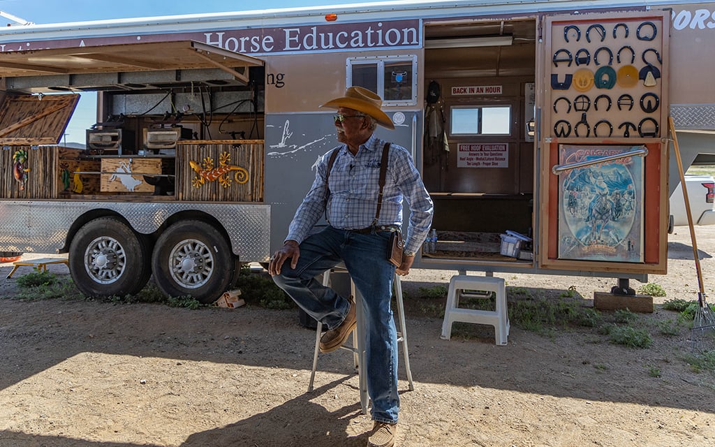 George Goode sits in front of his trailer on the Tohono O’odham Nation on April 10, 2024. Goode bought his trailer 30 years ago when the Native American Horse Education Foundation was still a dream. Now, he uses the trailer daily to help teach equine education to Native Americans. It houses materials necessary for horseshoeing, including burners, anvils, nails and shoes. (Photo by Sam Ballesteros/Cronkite News)