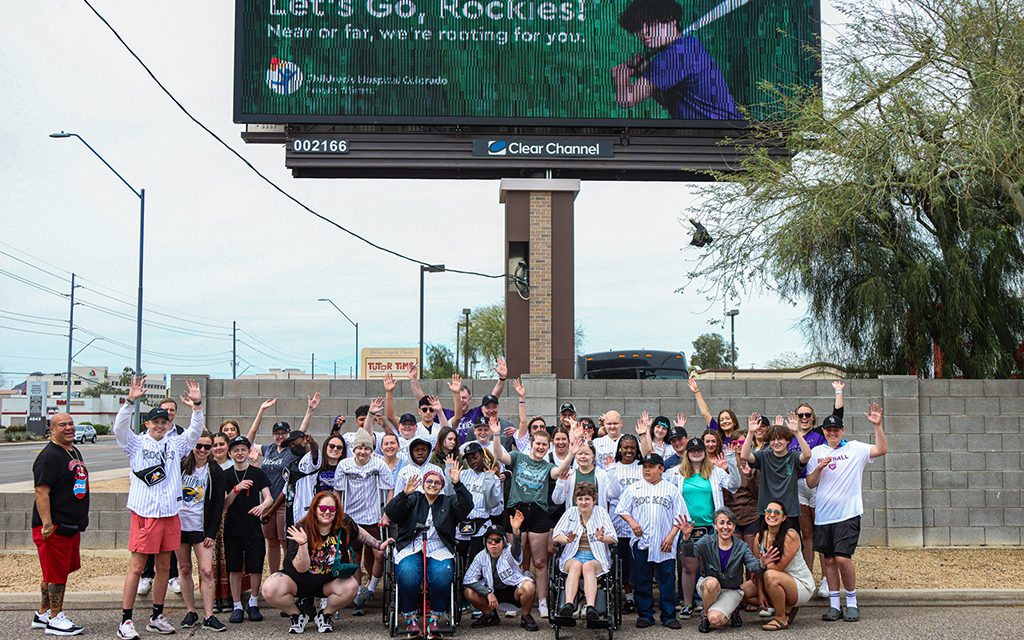 Patients from the Children’s Hospital Colorado cancer division pose in front a billboard that represents their program, which helped them meet Colorado Rockies players during spring training. (Photo by Spencer Barnes/Cronkite News)