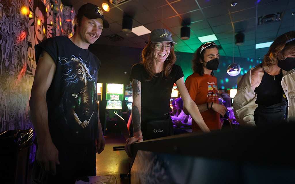 Todd Pearson, left, watches Katie Doyle play the Jaws pinball machine at Stardust Pinbar, on June 26, 2024. “I was never into it like he (Todd Pearson) was. I would just smash the buttons. He taught me there is a strategy to it, so now it’s a lot of fun.” Doyle said. (Photo by Stella Subasic/Cronkite News)