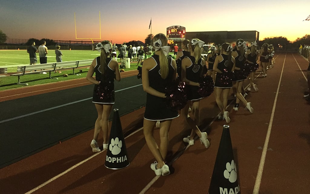 Desert Mountain cheerleaders stand during the national anthem before a football game. Even the cheerleaders’ short routines requires hours and hours of practice. (File photo by Brittany Bowyer/Cronkite News)