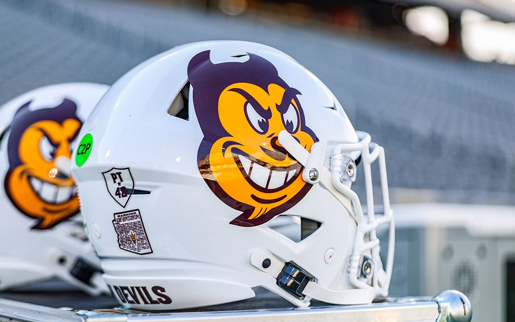 Close-up of two Arizona State football helmets with a Sun Devils design on the side. With a green dot on the back of the helmet indicates that the helmet is equipped with a communication device.