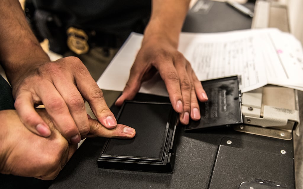 A close-up of a fingerprinting process with an officer pressing a person's thumb onto an ink pad.