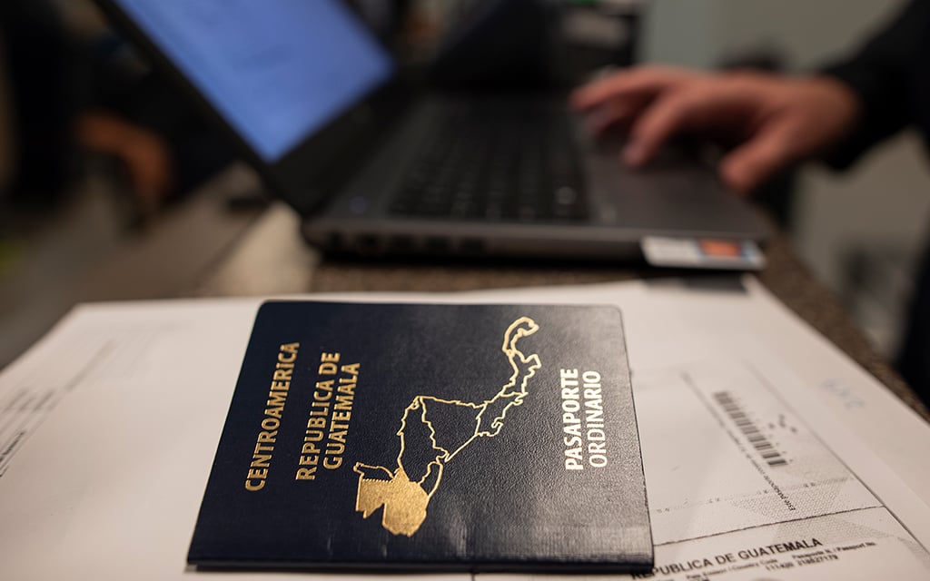 Guatemalan passport on a desk with a laptop and hands typing next to it.