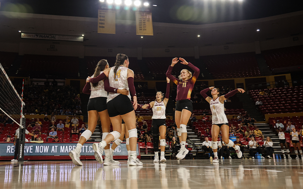 Arizona State volleyball players huddle together as Mary Shroll jumps in the air