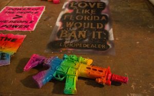 Colorful toy gun on a table with stencils and fabric pieces with text saying "Love like Florida Would Ban It" and "Power of the People > The people in Power."