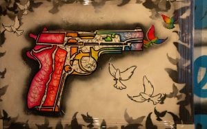 Street art of a multicolored handgun surrounded by black, white, and two colored doves on a beige background.