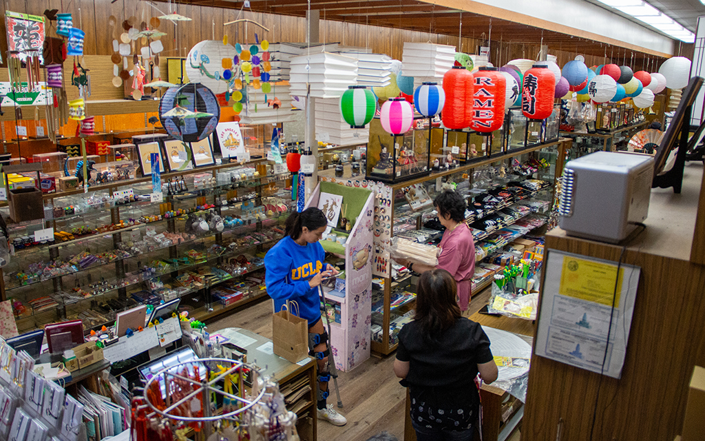 Interior of a Japanese goods store with glass display cases, colorful lanterns, and several customers browsing.