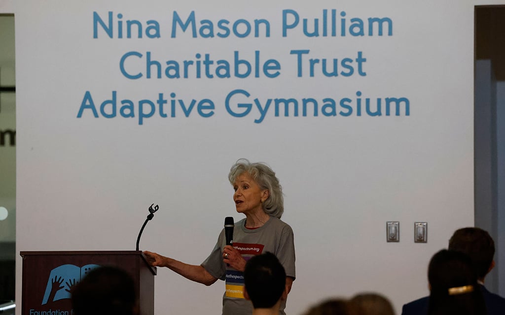 Desise Resnik speaking at a podium with large text on the wall behind her reading "Nina Mason Pulliam Charitable Trust Adaptive Gymnasium."