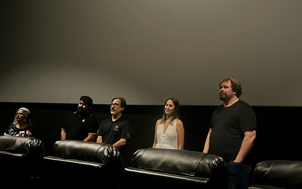 Cinco panelistas se paran frente a una pantalla vacía dentro de una sala de cine y comparten la historia de una película. 