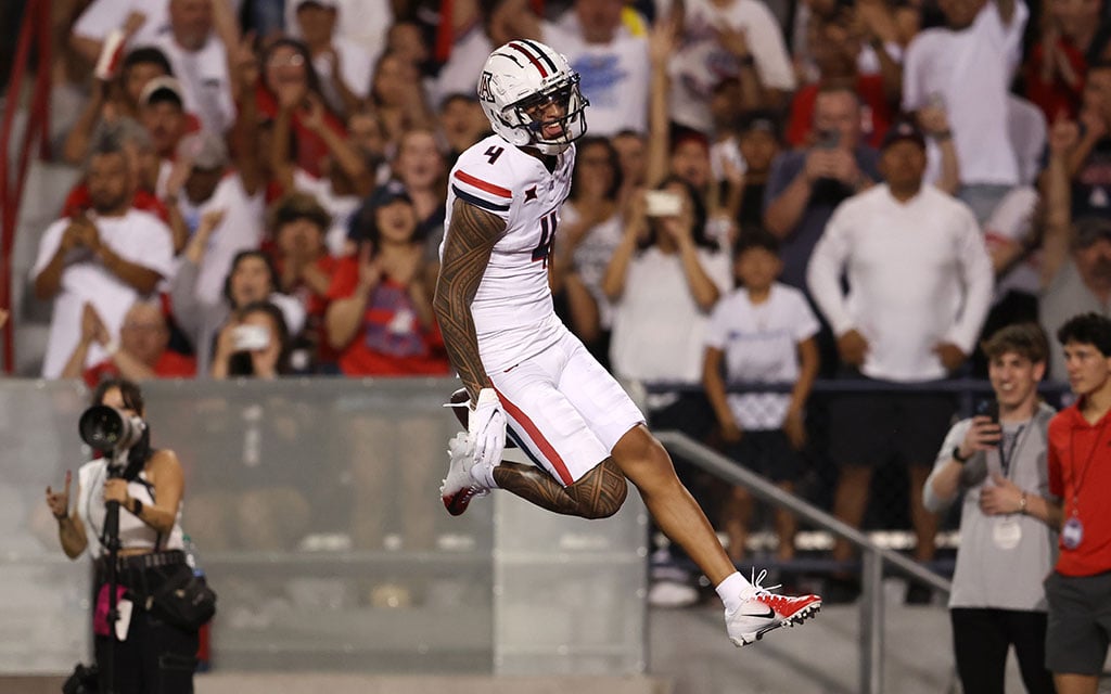 Tetairoa McMillan caught in mid-jump against a backdrop of an engaged audience and a field-side photographer.