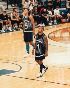 Isaiah Thomas and Paolo Banchero in black striped jerseys stand on the court during a game, with spectators seated in the background.