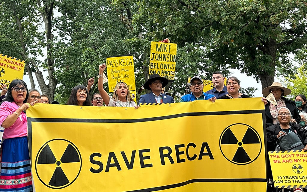 Protesters holding a yellow "SAVE RECA" banner and signs advocating for RECA passage.