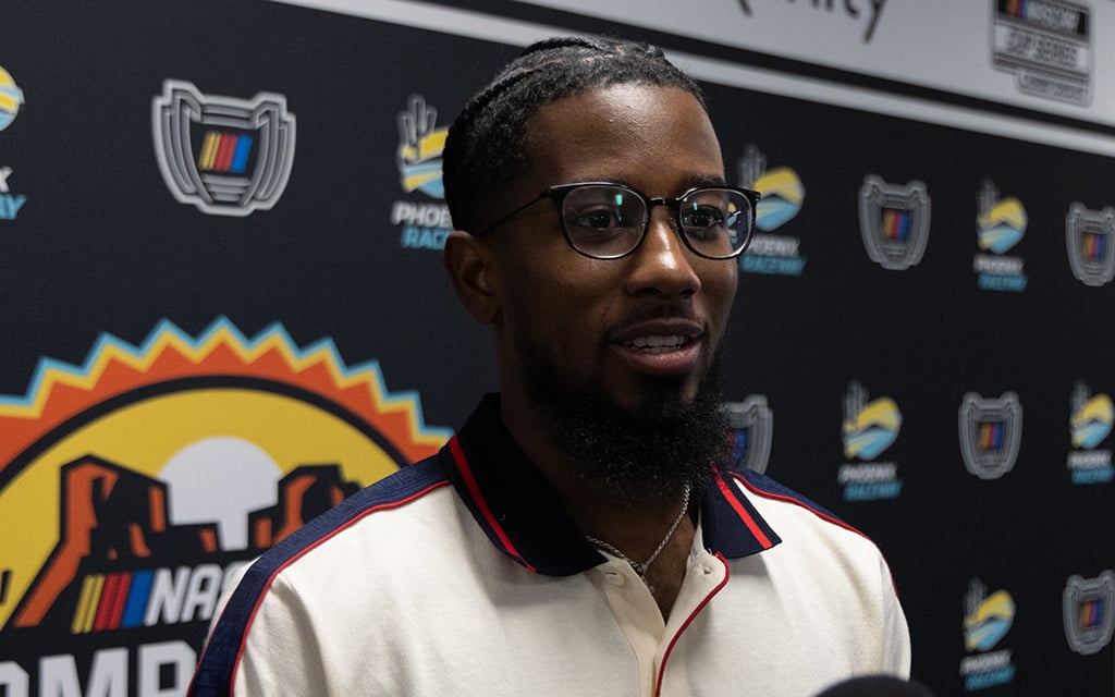 Rajah Caruth wearing glasses in front of a backdrop with racing logos.