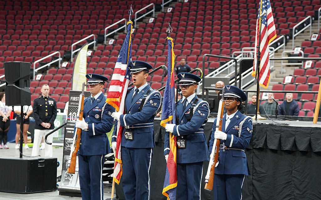 Four members of a color guard unit in blue dress uniforms standing in formation.