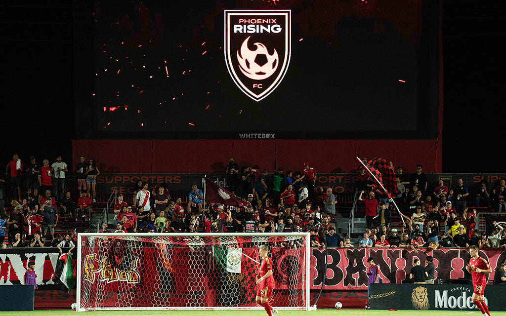 Soccer game at night with Phoenix Rising FC logo on a large screen and cheering fans in the background.