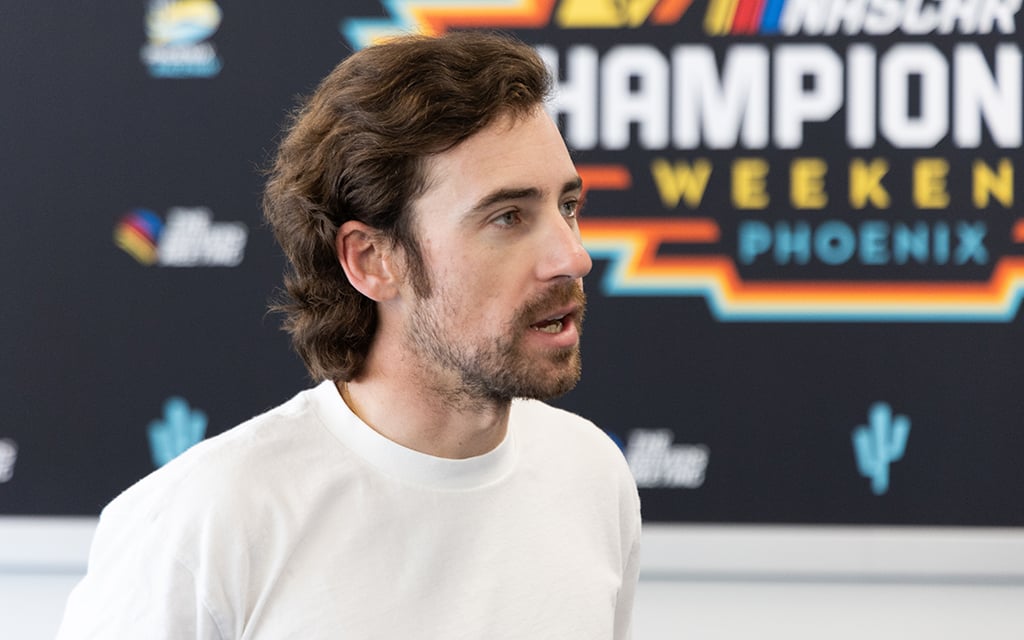 Ryan Blaney in a white T-shirt in front of a NASCAR Championship Weekend Phoenix promotional banner.