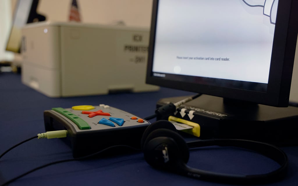 Close-up of an electronic voting machine controller and a monitor displaying text in a voting setup.