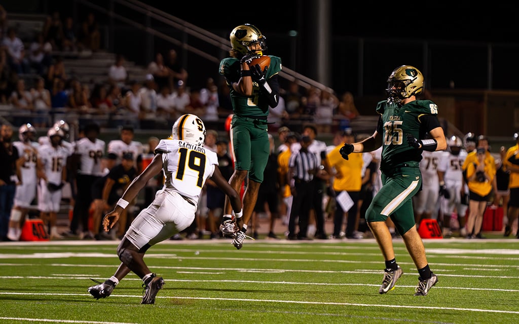 Gio Richardson leaping over opponent with football in his hand in football stadium.