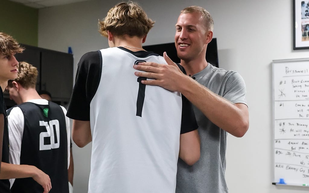 A man in a grey shirt pats the back of another man wearing a jersey with the number "1."