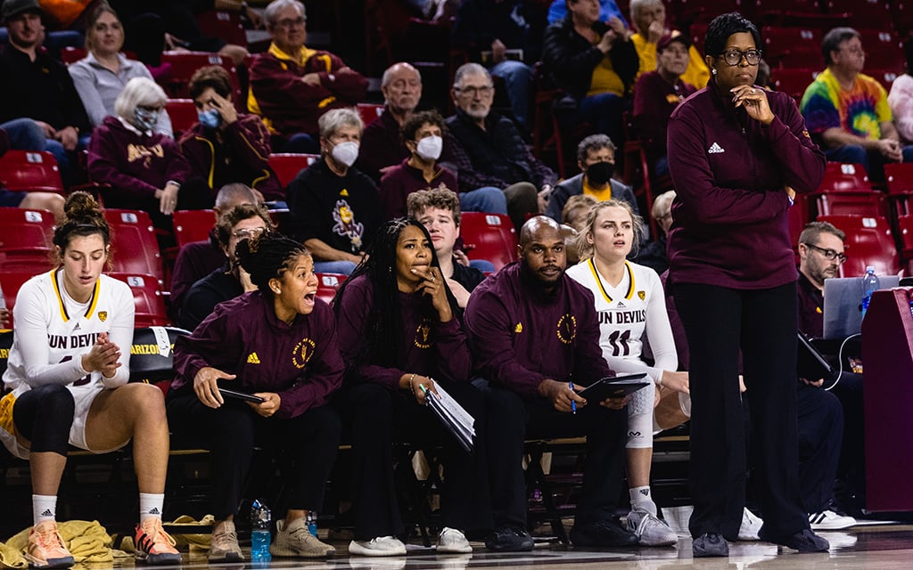 A group of people in sports attire on the sidelines with spectators in the background.